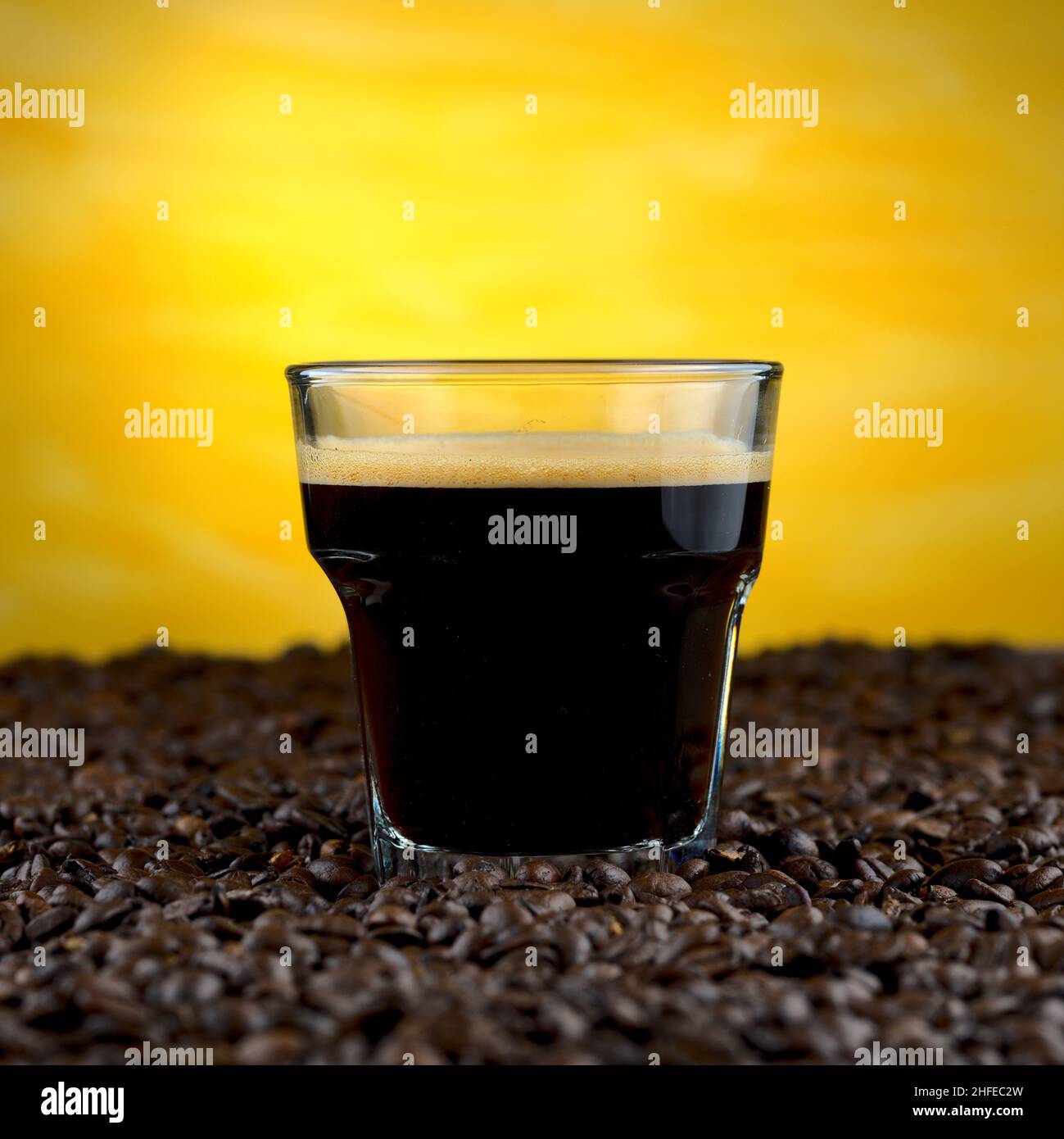 Espresso om Glas auf Kaffeebohnen auf gelbem Hintergrund Stockfoto