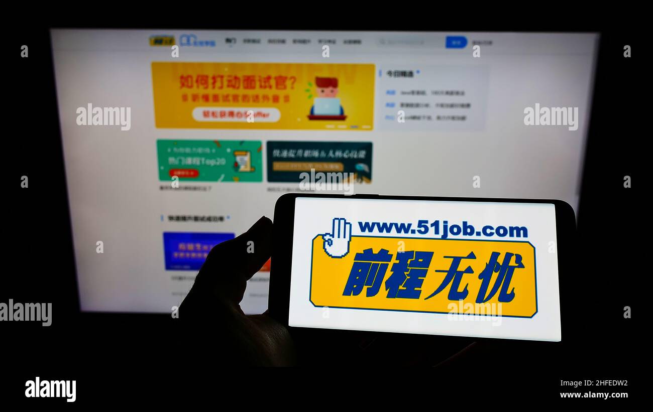 Person, die Mobiltelefon mit dem Logo des chinesischen Personalunternehmens 51job Inc. Auf dem Bildschirm vor der Geschäftswebseite hält. Konzentrieren Sie sich auf die Telefonanzeige. Stockfoto