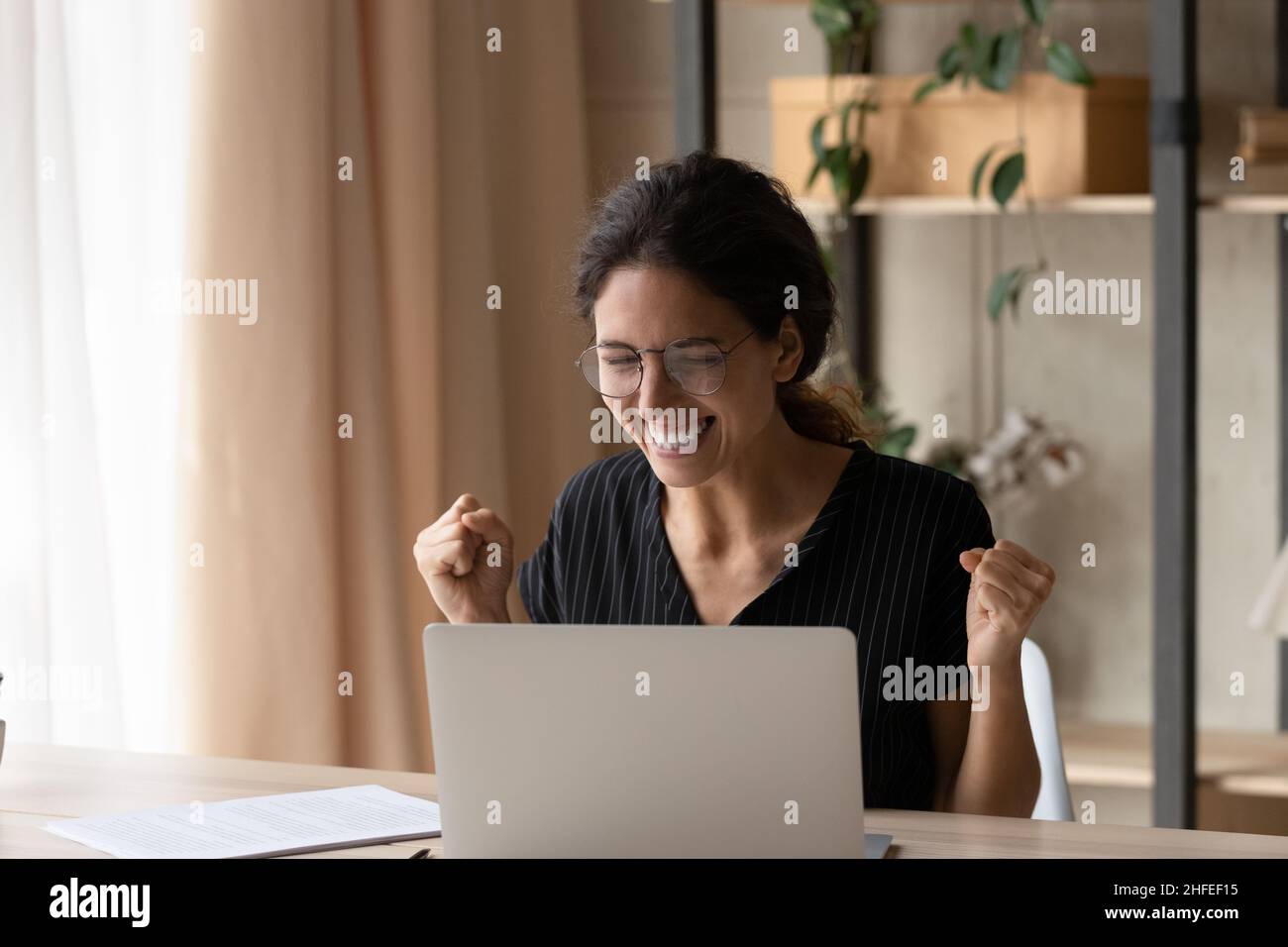 Emotionale, fröhliche junge Frau, die Online-Erfolg feiert. Stockfoto