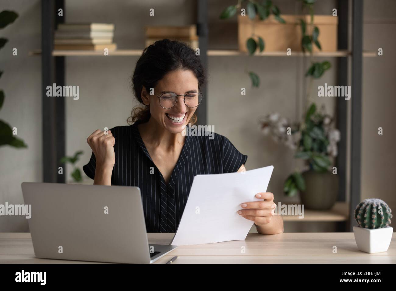 Fröhliche junge Frau, die Erfolg feiert, liest Papierbrief. Stockfoto