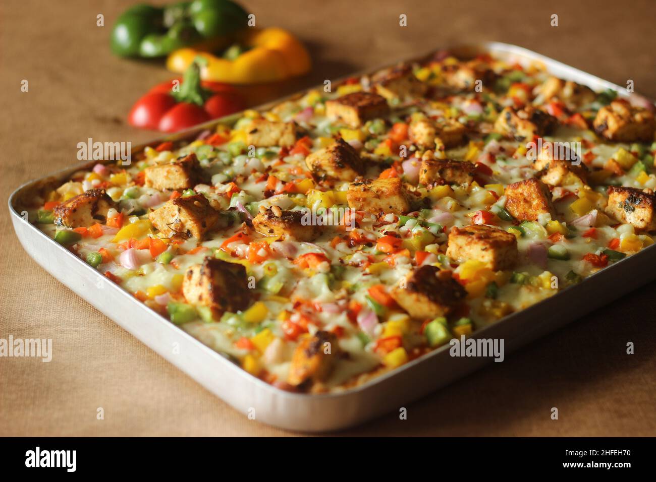 Hausgemachte Pizza mit Paneer, Mozzarella-Käse, rot-gelb-grünen Kapsikken und Zwiebeln. Gebacken in einem rechteckigen Tablett Stockfoto