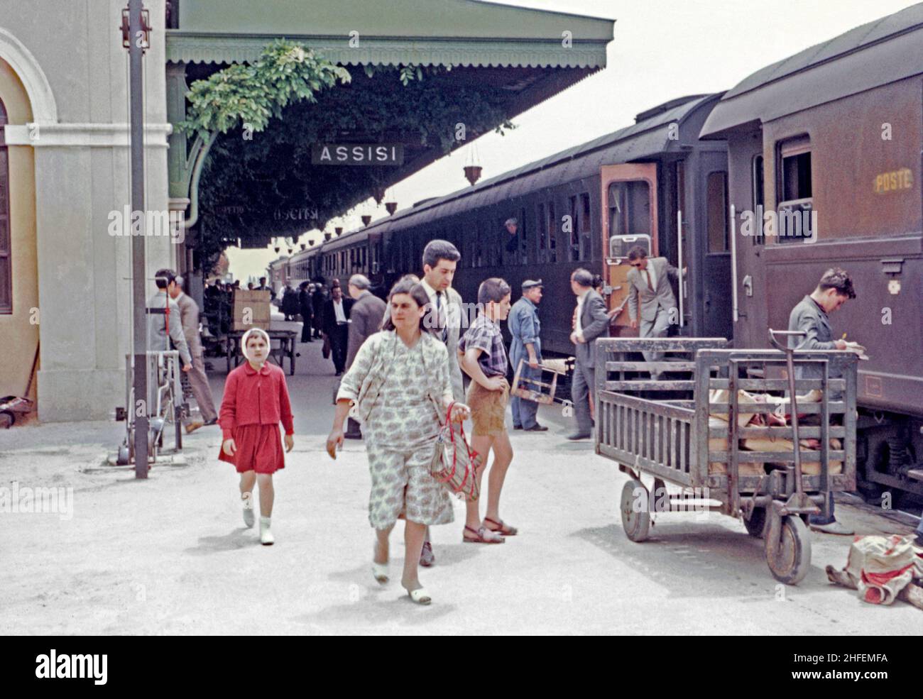Die Passagiere steigen um 1960 aus einem Zug am Bahnhof Assisi, Assisi, Umbrien, Italien, aus. Post (poste) wird auch mit der Bahn mit Taschen auf einem Handwagen (rechts) transportiert. Der Bahnhof von Assisi befindet sich an der Piazza Dante Alighieri, Santa Maria degli Angeli, etwa 5 Kilometer südwestlich des Stadtzentrums. Der Bahnhof wurde 1866 eröffnet und ist Teil der Bahn Foligno-Terontola, die auch Florenz mit Rom verbindet. Dieses Bild stammt von einem alten Amateur 35mm Farbtransparenz – ein Vintage 1950/60s Foto. Stockfoto