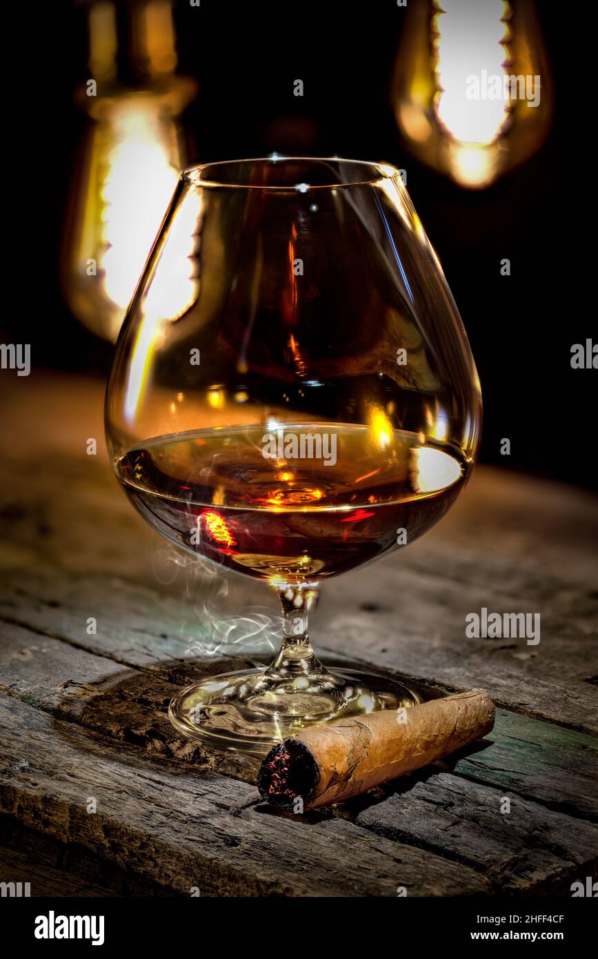 Cognac und Zigarre auf einem alten Holztisch und einem Hintergrund mit Vintage-Lampen Stockfoto