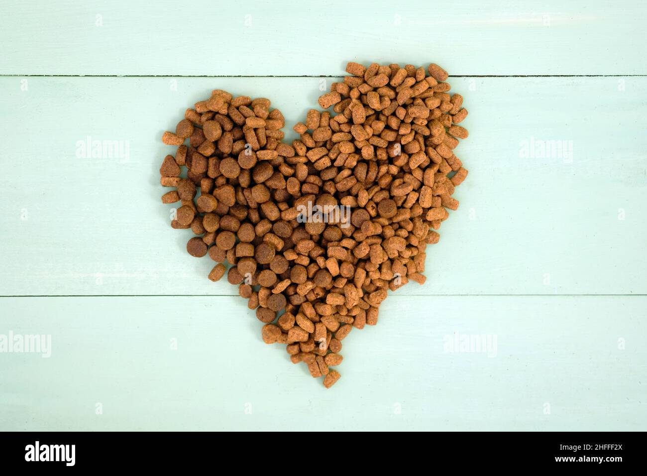 Trockenfutter für Hunde und Katzen auf einem Holz bemalten Hintergrund Draufsicht. Trockenes Tierfutter, das in Form eines Herzens ausgelegt ist. Stockfoto