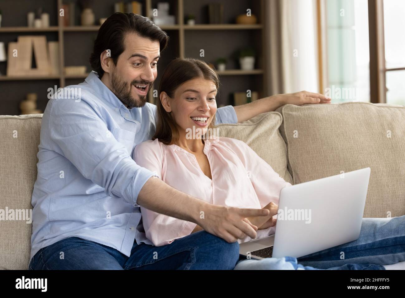 Ein Paar, das auf den Laptop-Bildschirm schaut, liest großartige Nachrichten, fühlt sich erstaunt Stockfoto