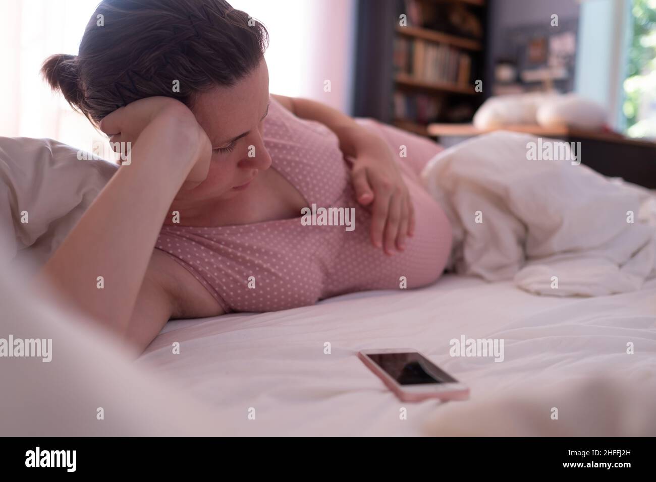 Kaukasische Frau mit Telefon, die zu Hause auf dem Sofa Wehen hat und atmet Stockfoto