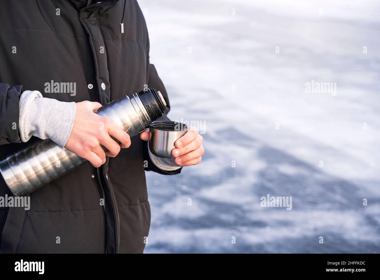 Junger Mann, Teenager gießt und trinkt den heißen Tee aus Thermoskannen am Winterstrand des kalten gefrorenen Baikalsees, Menschen und gesunde Lebensweise con Stockfoto