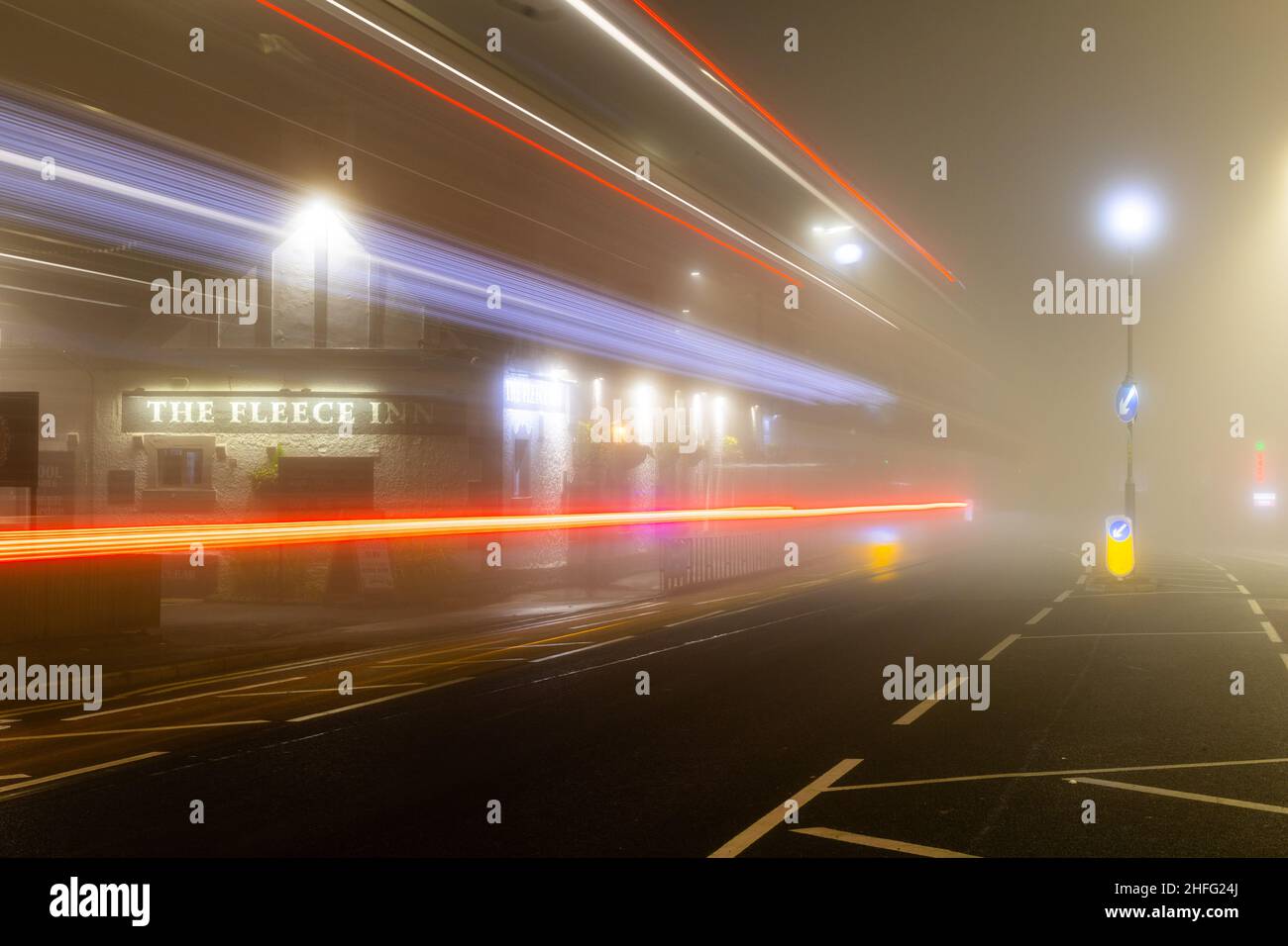 Das Fleece Inn, ein britischer Pub, schoss im Morgennebel und zeigte leichte Streifen vorbeifahrenden Autos. Stockfoto