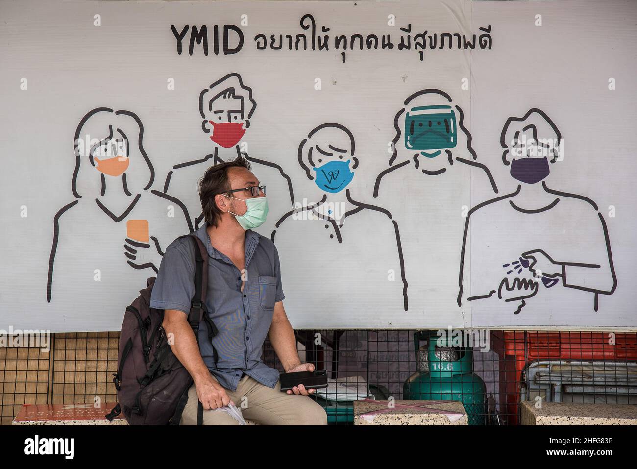 Bangkok, Thailand. 16th Januar 2022. Ein Mann mit Gesichtsmaske als vorbeugende Maßnahme gegen die Verbreitung von covid-19 sitzt in der Nähe eines Werbebanners am Victory Monument in Bangkok. Kredit: SOPA Images Limited/Alamy Live Nachrichten Stockfoto