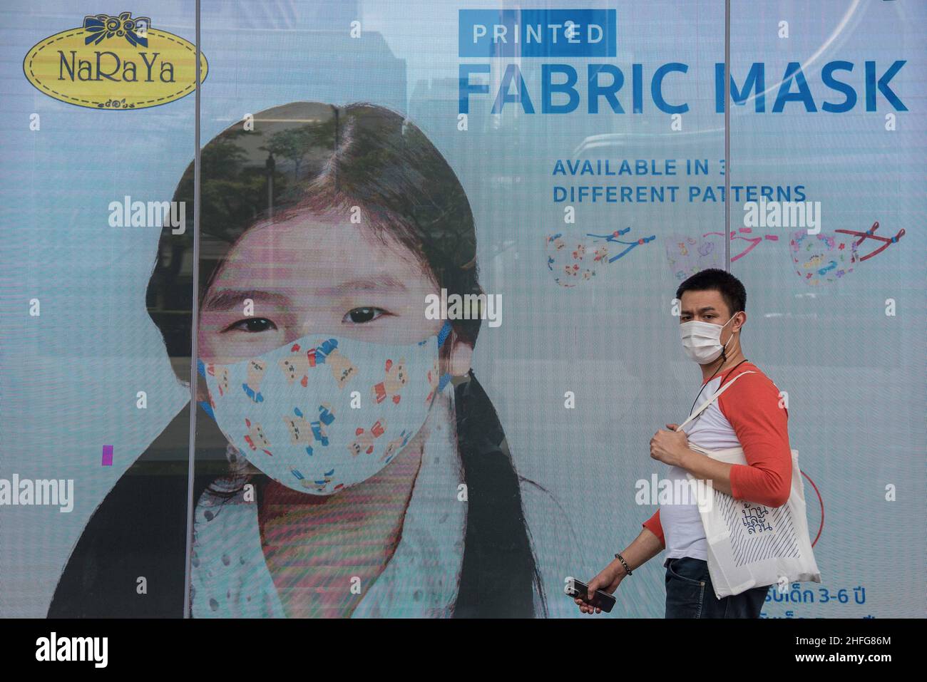 Bangkok, Thailand. 16th Januar 2022. Ein Mann, der eine Gesichtsmaske als vorbeugende Maßnahme gegen die Ausbreitung von covid-19 trägt, geht an einem Werbebildschirm vorbei, der außerhalb der Central World, dem Einkaufszentrum in Bangkok, Thailand, angezeigt wird. Kredit: SOPA Images Limited/Alamy Live Nachrichten Stockfoto