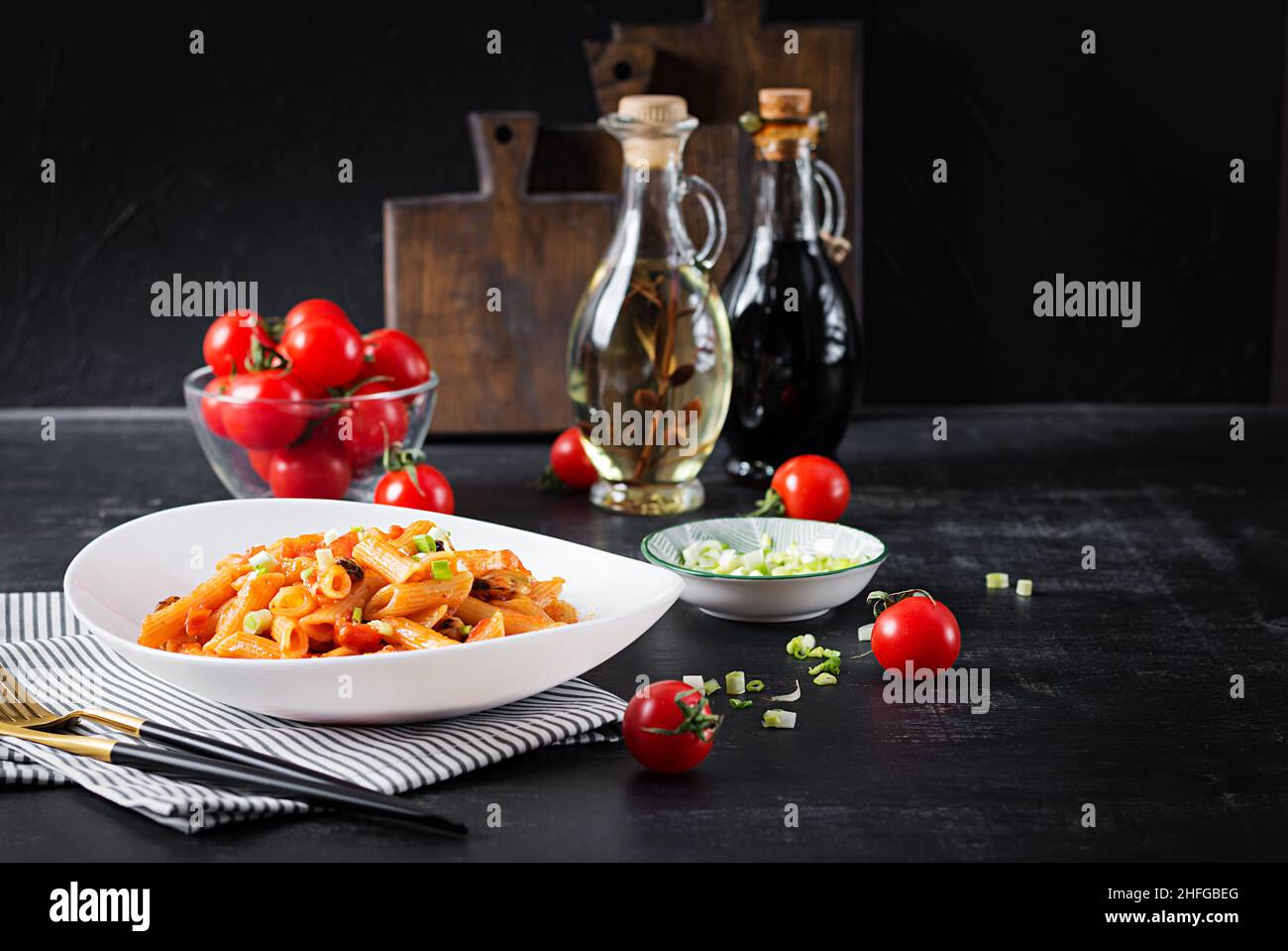 Klassische italienische Pasta Penne Marinara mit Muscheln und grünen Zwiebeln auf dunklem Tisch. Penne mit Sauce Marinara. Stockfoto