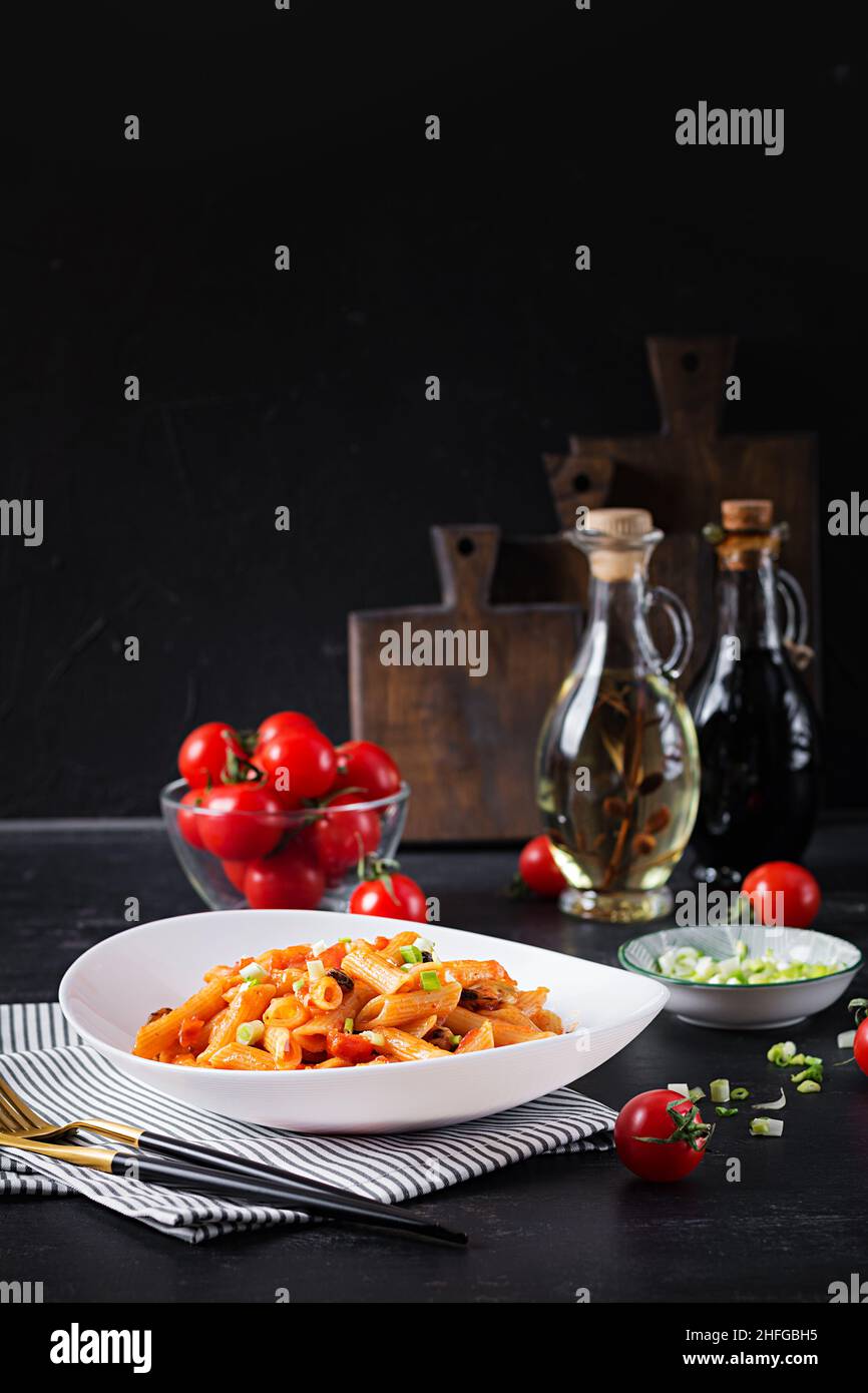 Klassische italienische Pasta Penne Marinara mit Muscheln und grünen Zwiebeln auf dunklem Tisch. Penne mit Sauce Marinara. Stockfoto