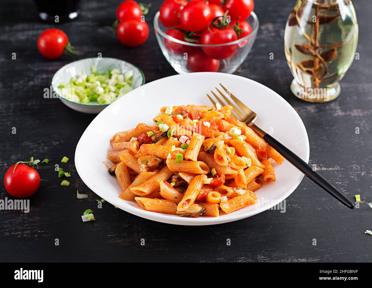 Klassische italienische Pasta Penne Marinara mit Muscheln und grünen Zwiebeln auf dunklem Tisch. Penne mit Sauce Marinara. Stockfoto
