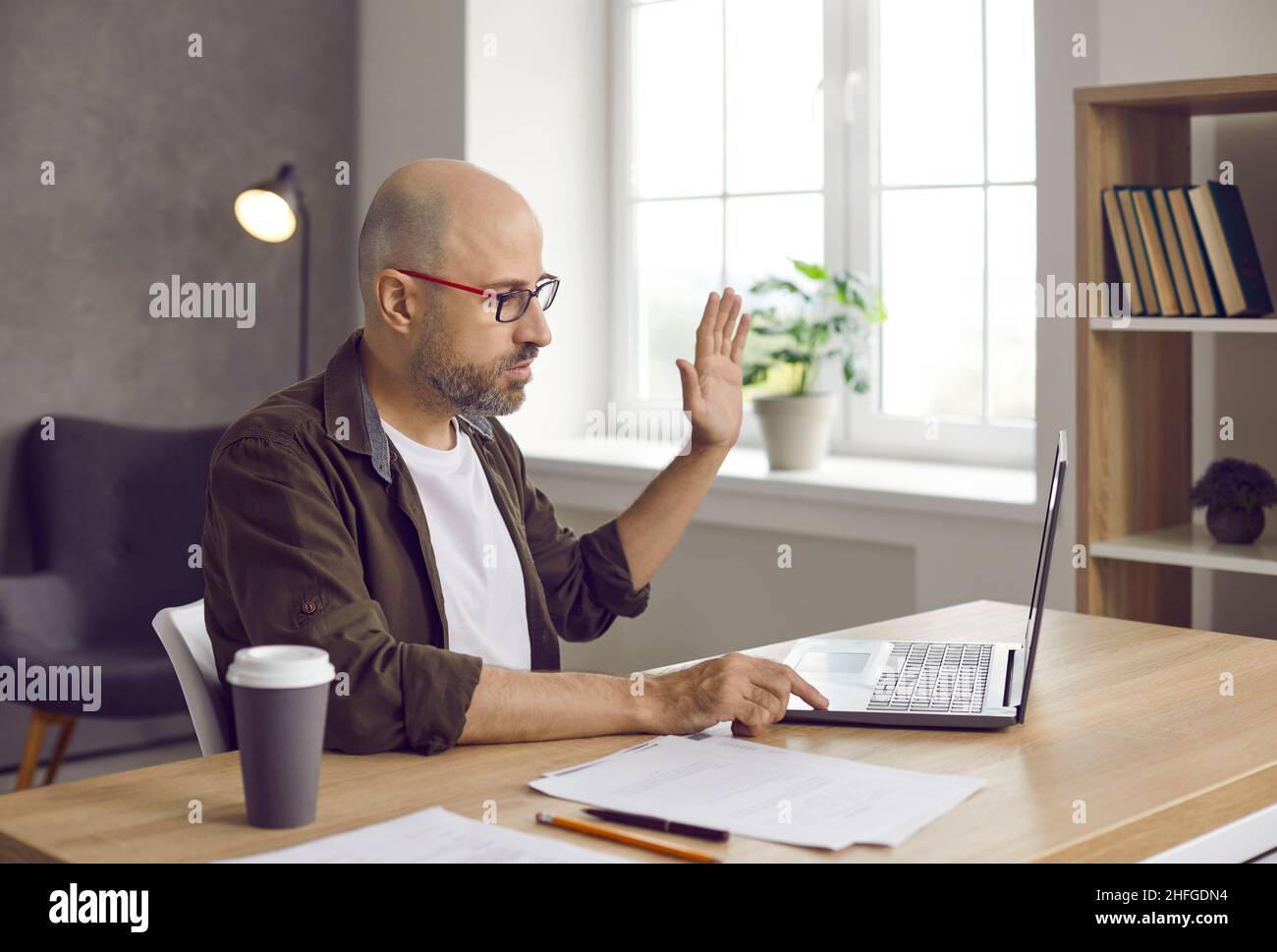 Geschäftsmann winkt mit der Hand vor der Webcam des Laptops und begrüßt den Kunden bei einem Videoanruf. Stockfoto