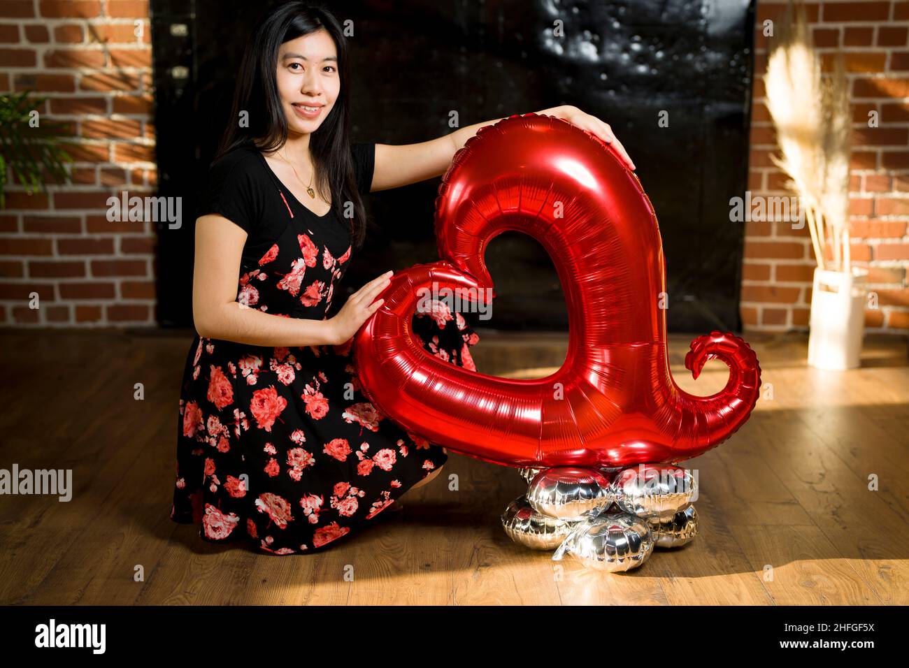 Junge ostasiatische Frau mit großer Ballonskulptur am Roten Valentinstag sitzend Stockfoto