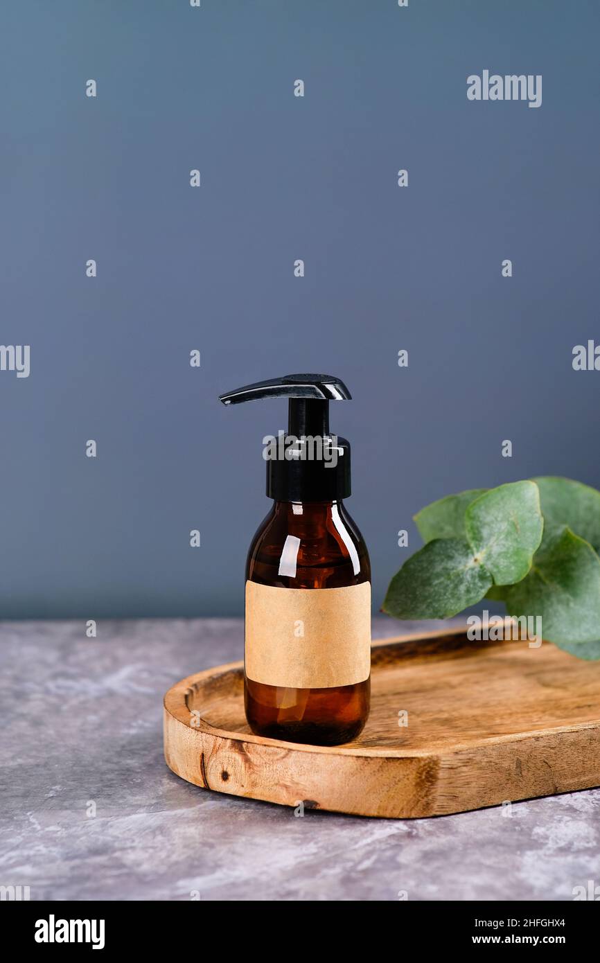 Dunkle bernsteinfarbene Glasflasche mit Duschgel oder Shampoo auf Holzbrett mit Eukalyptusblättern. SPA natürliche organische Schönheit Produkt, Kosmetik-Verpackung des Stockfoto