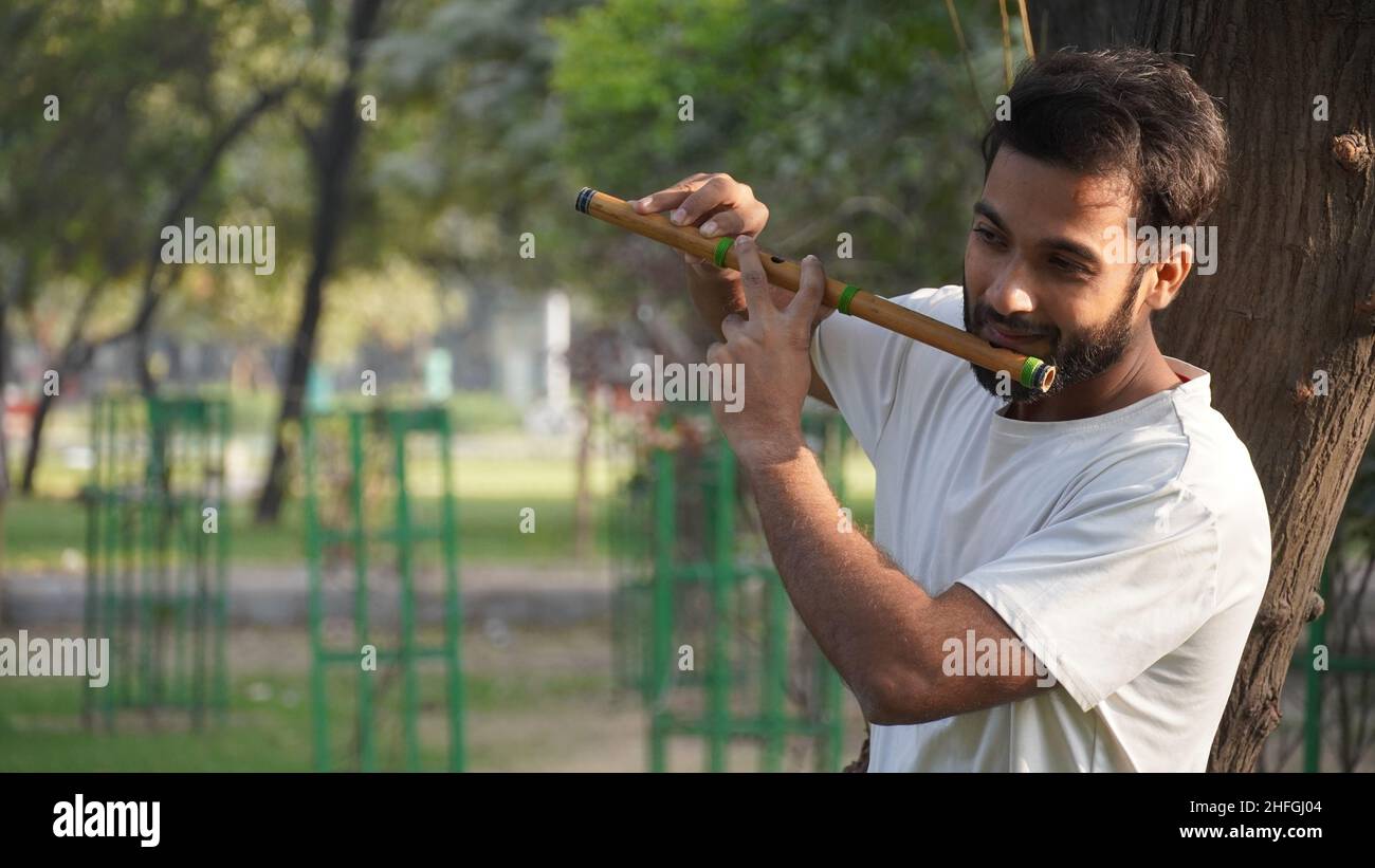 Bansuri-Spieler, der bei Sonnenschein im Park Musik spielt - Indian Flute Player Stockfoto