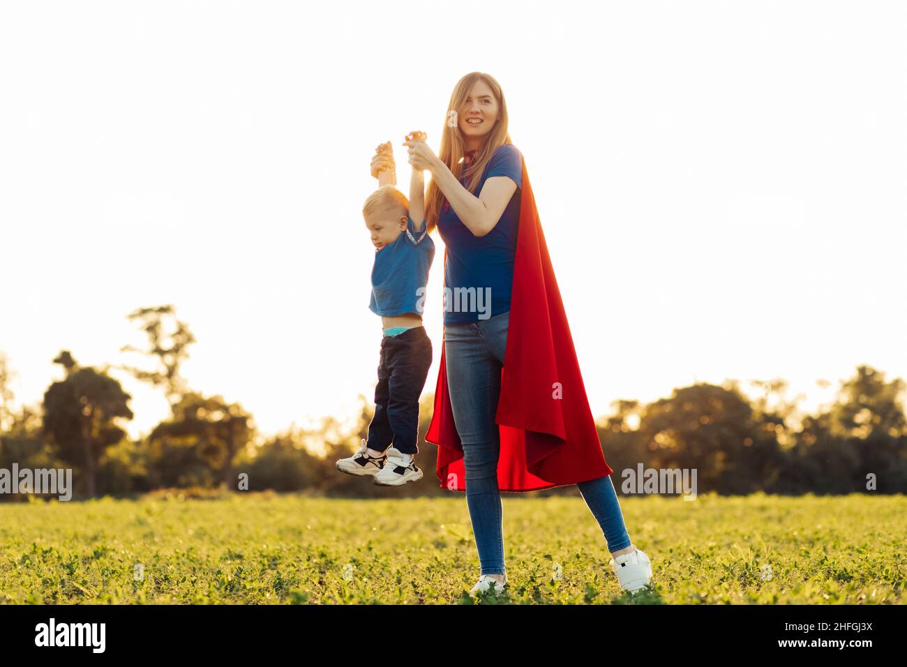 Mutter und ihr Kind spielen im Freien zusammen. Mutter und Sohn in Superhelden-Kostümen. Mama und Baby haben Spaß, lächeln und umarmen. Familienurlaub und Zweisamkeit Stockfoto