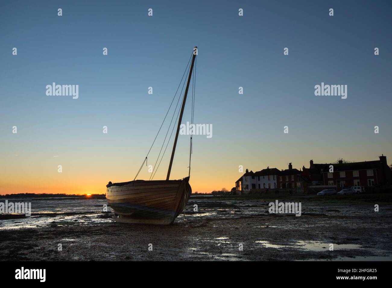 Bosham, Hafen von Bosham, mit Holzyacht, die auf dem Rumpf neben Dorfhäusern ruht, Sonnenuntergang, Dämmerung, Gezeiten, Sussex, Großbritannien, Januar. Stockfoto