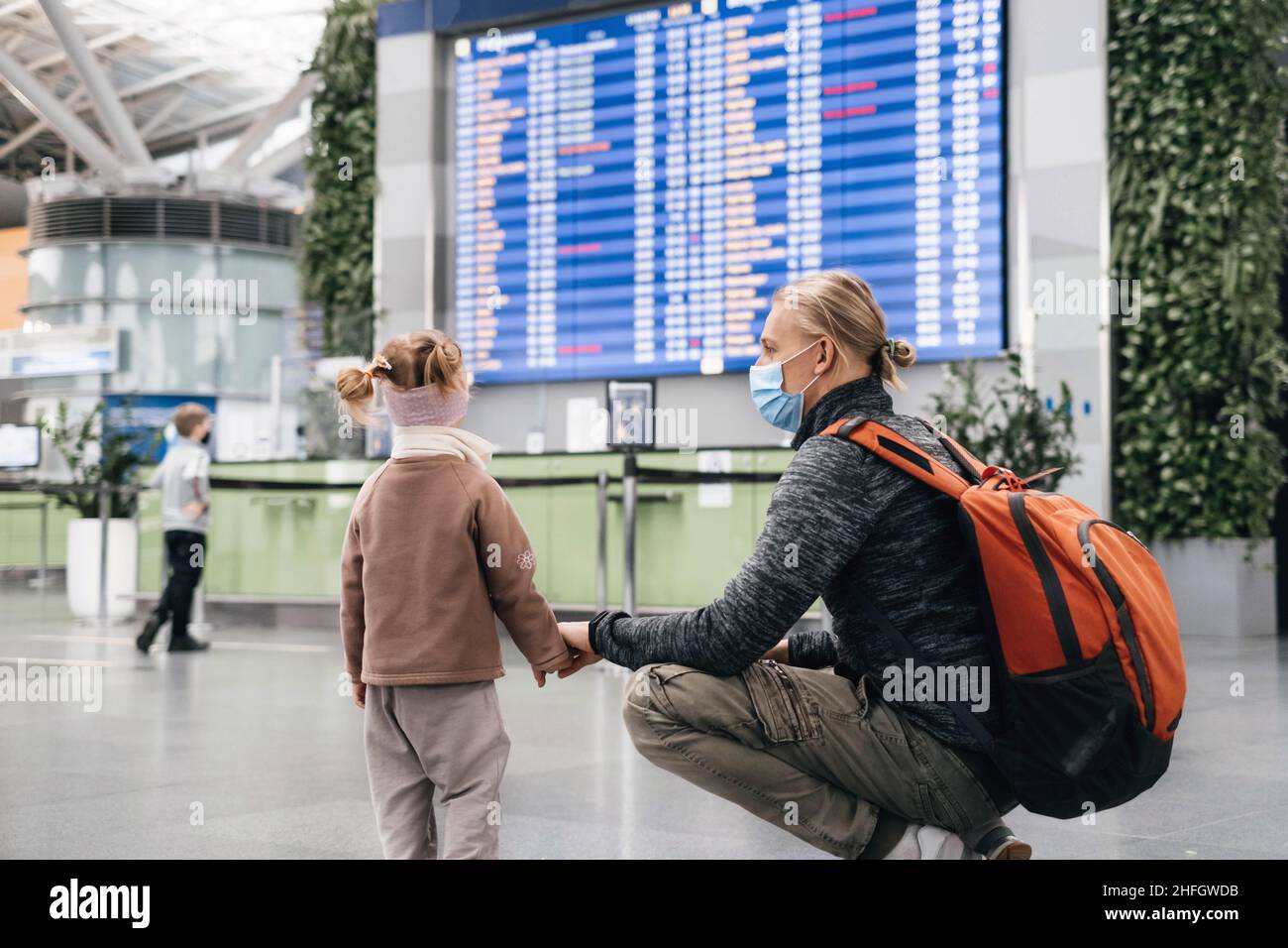 Mann und Mädchen sehen sich die Flugplaninformationen am Flughafen an, Passagiere warten auf ein Flugzeug. Familienreise mit dem Flugzeug. Flugverspätung Stockfoto