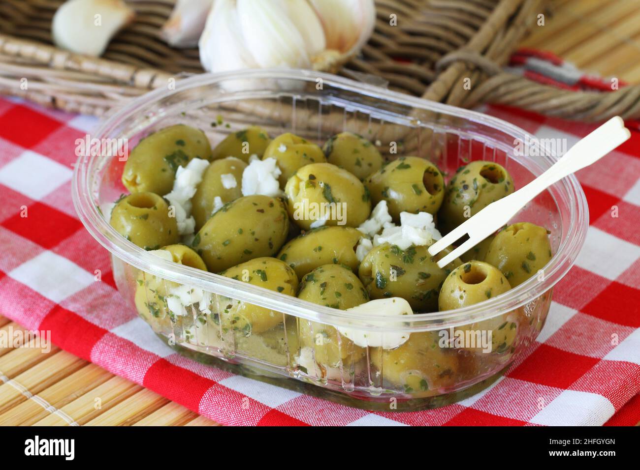 Frische grüne Oliven mit Knoblauch in transparenter Kunststoffbox auf kariertem Tuch Stockfoto