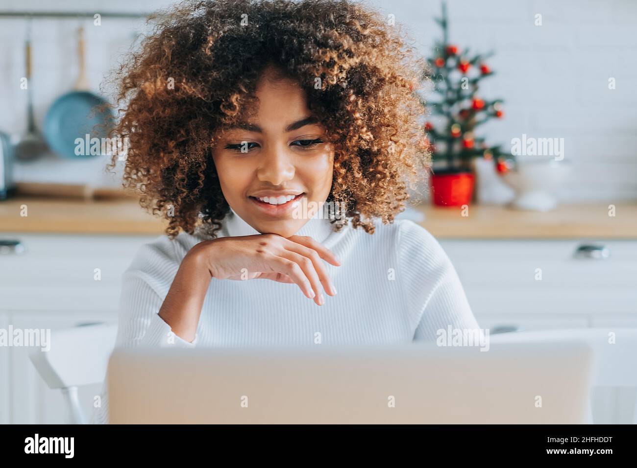 Konzentrierter und aufgeregter, dunkelhäuter junger Käufer mit trendigen Haaren lächelt im Laptop und genießt Online-Shopping in Nahaufnahme Stockfoto