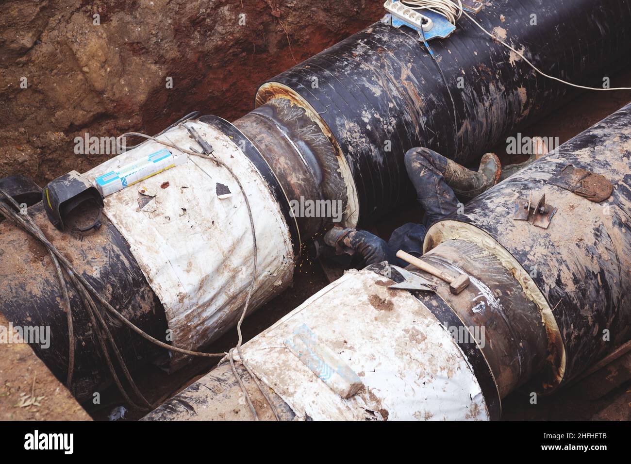 Reparatur des Heizkanals. Die Arbeiter, Schweißer, die durch Elektroschweißen und Gasschweißen an großen Eisenrohren in einer Tiefe von ausgegrabenen Graben hergestellt wurden. Stockfoto