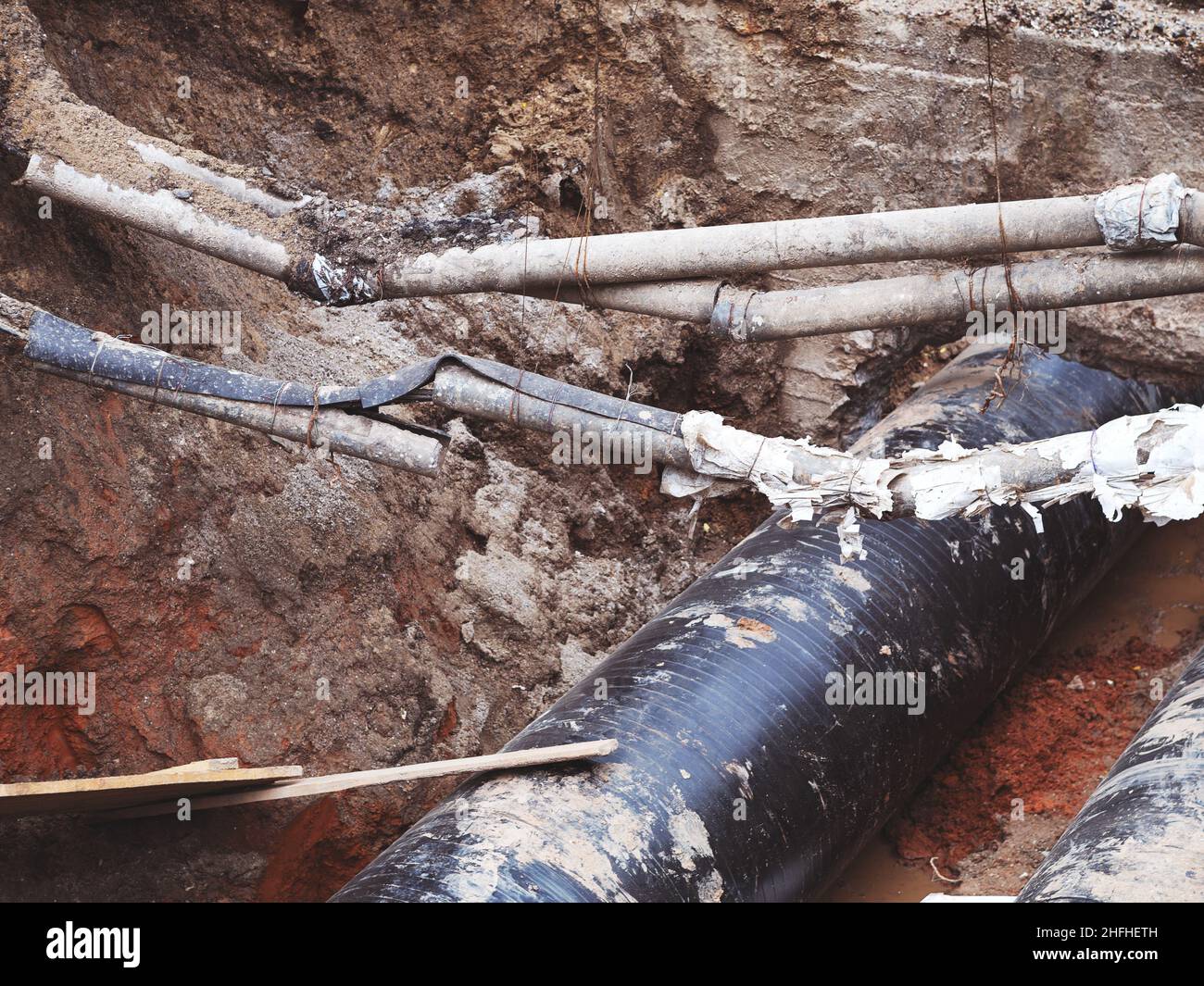 Reparatur des Heizkanals. Große Eisenrohre in einer Tiefe des ausgegrabenen Grabens. Stockfoto