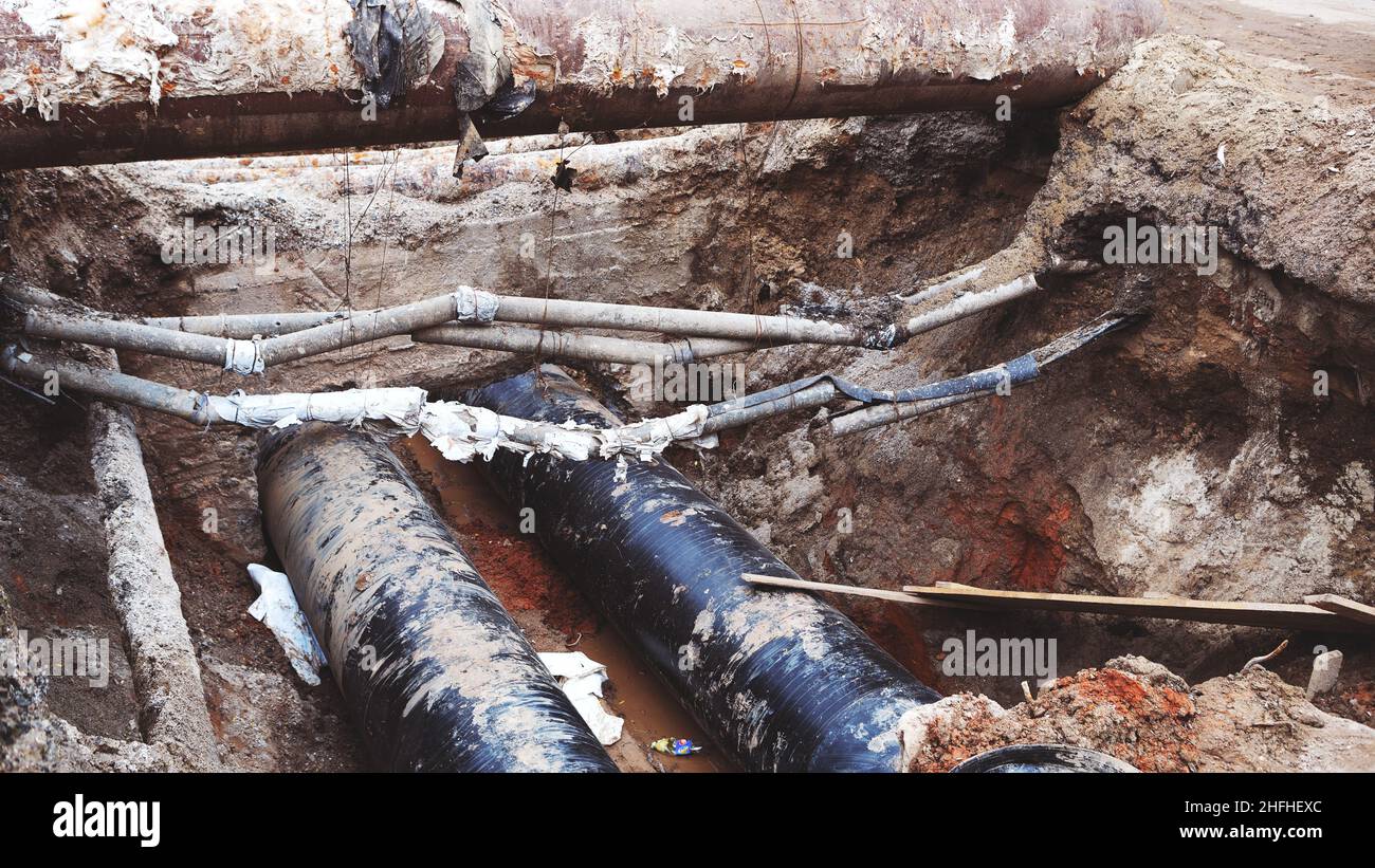 Reparatur des Heizkanals. Große Eisenrohre in einer Tiefe des ausgegrabenen Grabens. Stockfoto