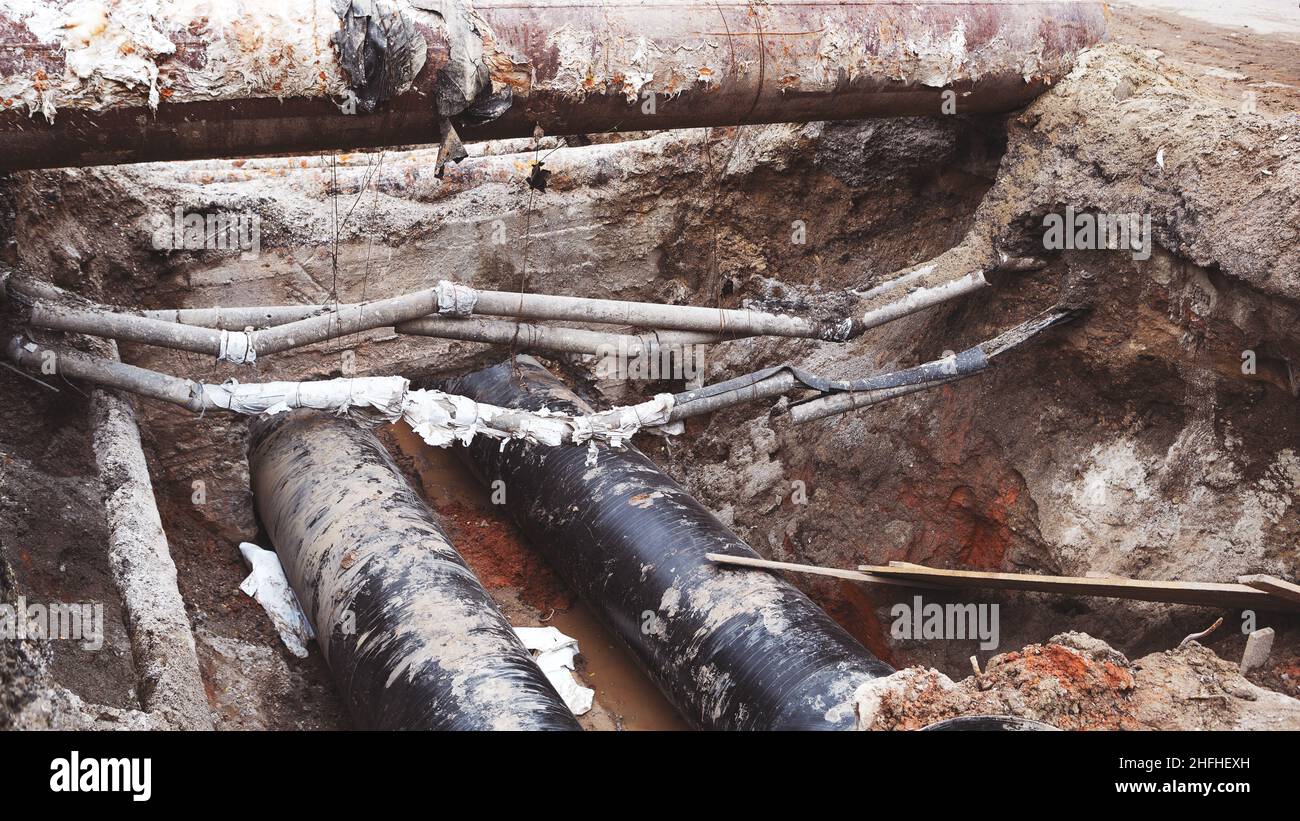 Reparatur des Heizkanals. Große Eisenrohre in einer Tiefe des ausgegrabenen Grabens. Stockfoto