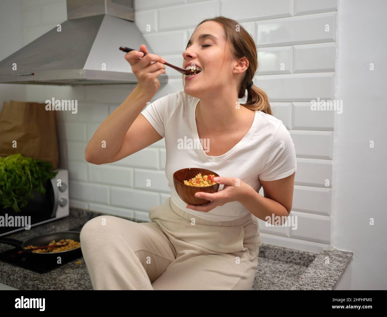 Frau nimmt Nahrung von ihrer Gabel, um sie in den Mund zu legen und isst lässig auf der Arbeitsplatte Stockfoto