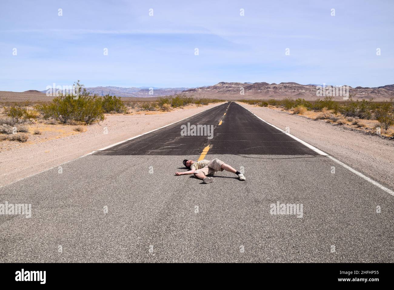 Ein Mann, der vorgibt, regungslos mitten auf einer Autobahn im Death Valley, USA, zu liegen Stockfoto