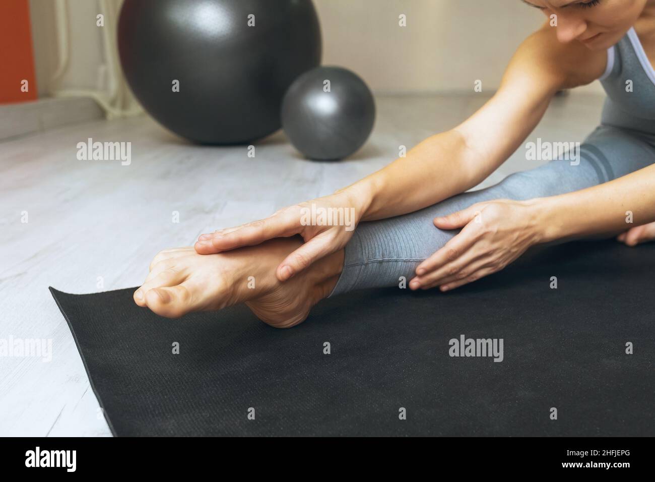 Eine Frau führt eine Knöcheldehnung durch, sitzt auf einer Gymnastikmatte im Studio Stockfoto