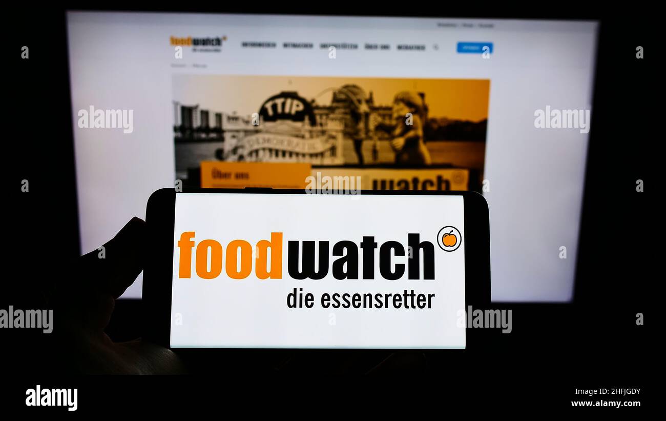 Person, die Mobiltelefon mit Logo der deutschen Interessenvertretung Foodwatch e.V. auf dem Bildschirm vor der Webseite hält. Konzentrieren Sie sich auf die Telefonanzeige. Stockfoto