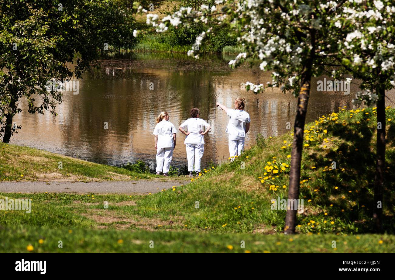 Umea, Norrland Schweden - 10. Juni 2020: Drei Krankenschwestern haben während der Pandemie an einem kleinen See eine Pause Stockfoto