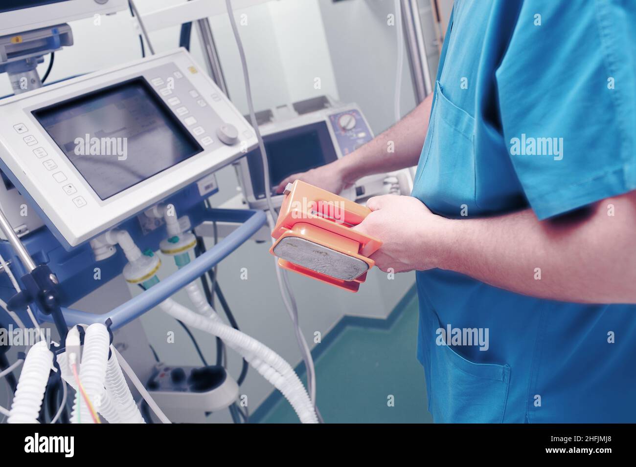 Der männliche Arzt mit Defibrillatorelektroden in der Hand stellt die elektrischen Entladungsparameter vor dem Monitor für die Lebenserhaltungssupport ein. Stockfoto