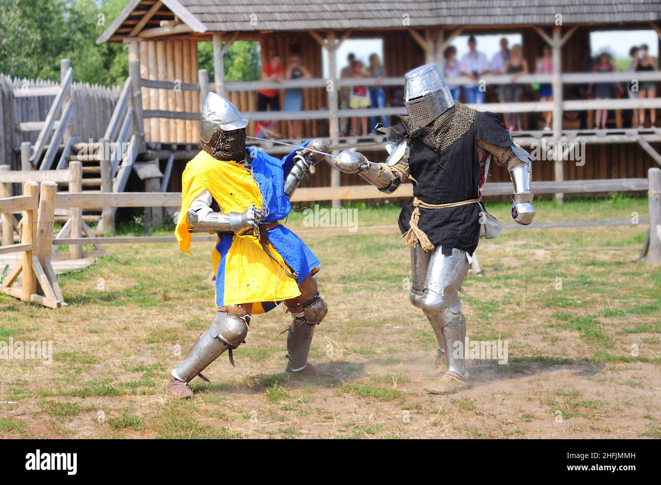 Zwei Ritter kämpfen in Rüstung mit Schwertern, Rekonstruktion des Turniers. Eine Szene mit Zuschauern aus einem Blockhaus. Feier der heidnischen da Stockfoto