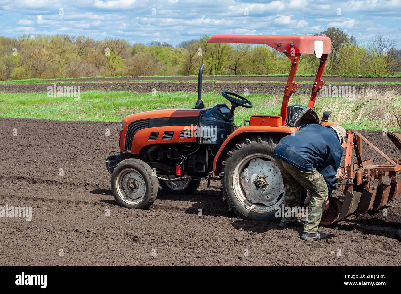 Frühling landwirtschaftliche Arbeit auf dem Feld, Pflanzung von Kartoffeln im Dorf. Roter kleiner Traktor mit Pflug und einem Mann von hinten. Stockfoto