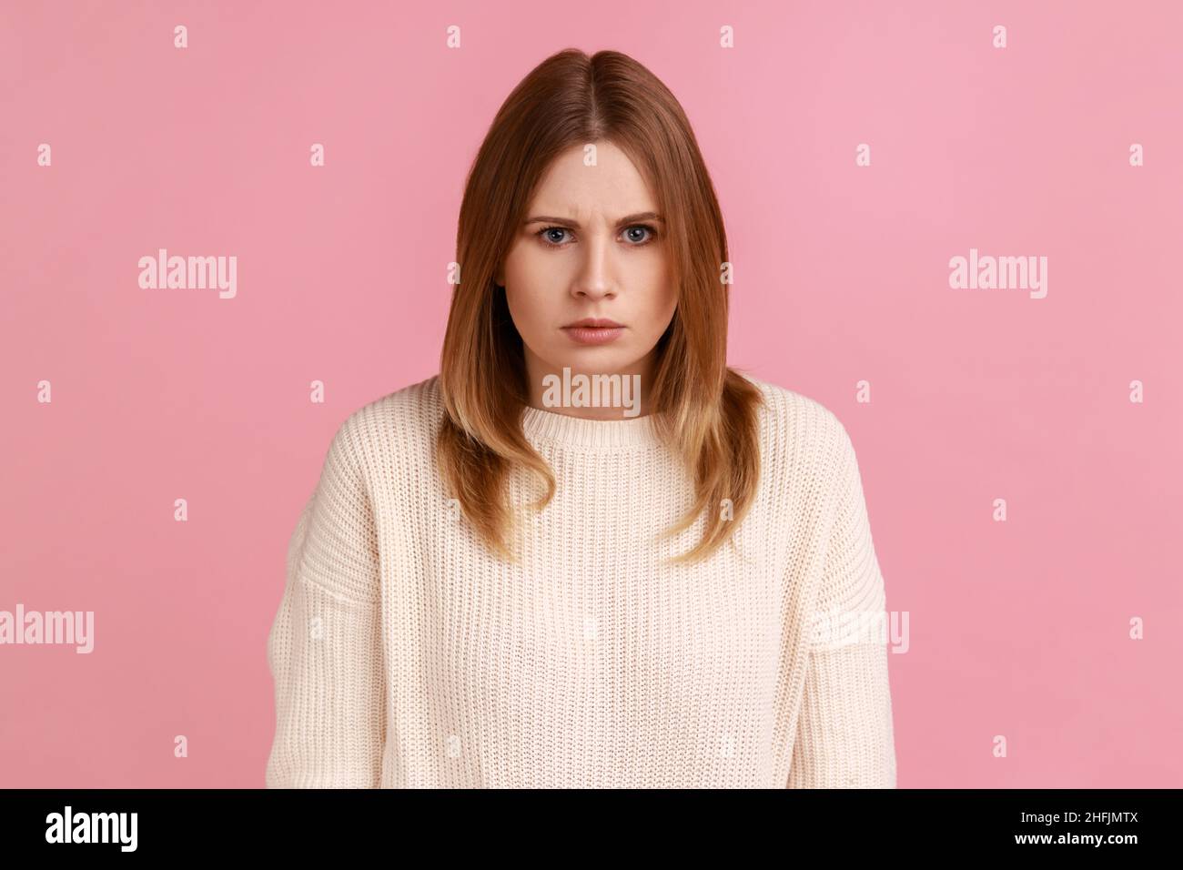Porträt eines jungen Erwachsenen wütend ernst blonde Frau Blick auf die Kamera mit strengen negativen Ausdruck, Aggression, trägt weißen Pullover. Innenaufnahme des Studios isoliert auf rosa Hintergrund. Stockfoto
