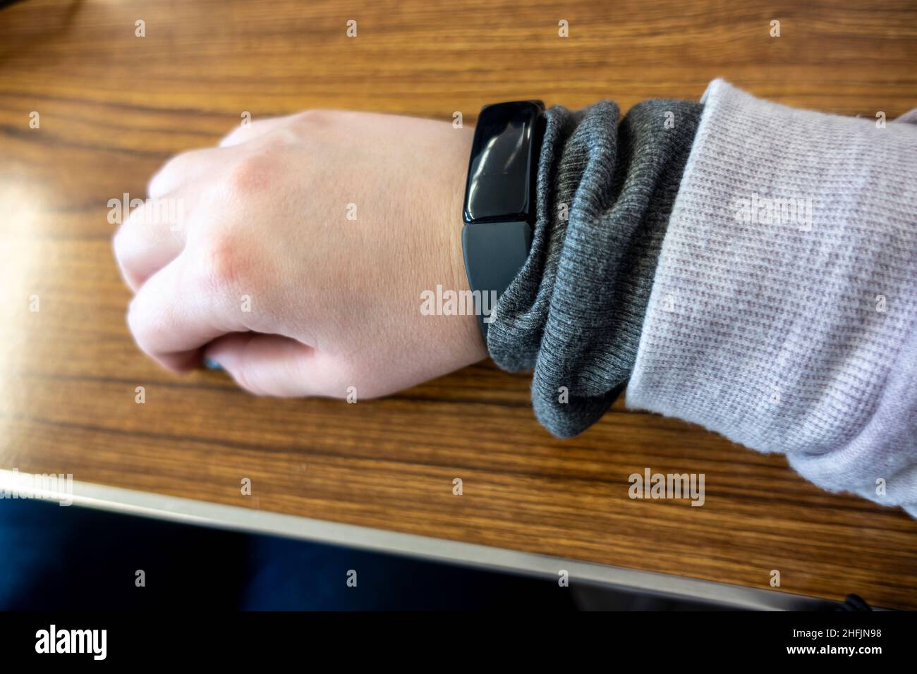Blick auf eine casukasische, weibliche Hand mit einem schwarzen Fitness-Tracker am Handgelenk, gegen einen Holztisch gestellt Stockfoto