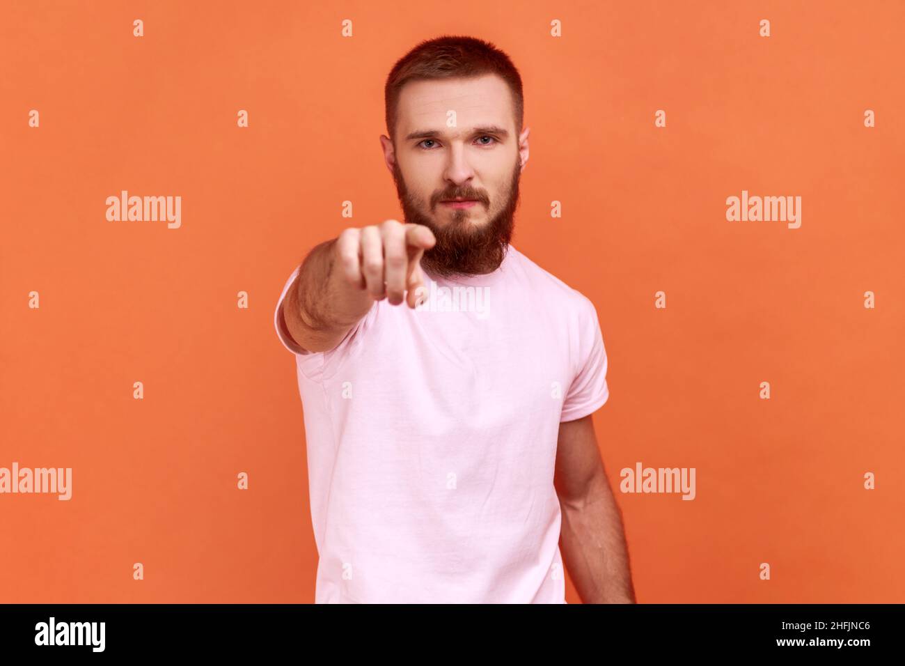 Porträt eines bärtigen Mannes, der wegen eines Fehlers schimpfte, unzufrieden mit dem Verhalten, beschuldigende Geste mit pinkfarbenem T-Shirt. Innenaufnahme des Studios isoliert auf orangefarbenem Hintergrund. Stockfoto