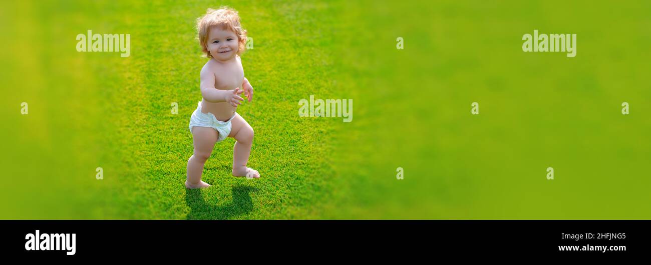 Banner mit Feder Kindergesicht. Erster Schritt. Baby steht barfuß auf dem grünen Rasen in Windelhosen. Kinder auf grünem Gras Hintergrund. Stockfoto