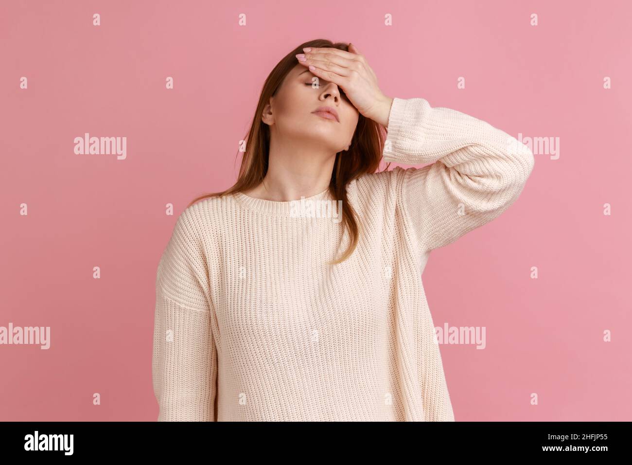 Porträt einer enttäuschten, frustrierten, blonden Frau, die eine Facepalm-Geste macht, schockiert, beschämt über Verlieren, Versagen, trägt einen weißen Pullover. Innenaufnahme des Studios isoliert auf rosa Hintergrund. Stockfoto