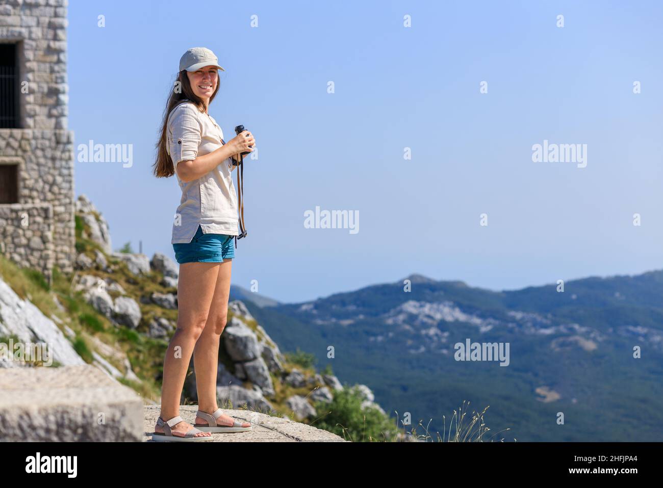 Junge Frau beobachtet die Berglandschaft durch ein Fernglas am Aussichtspunkt auf dem Touristenpfad Stockfoto