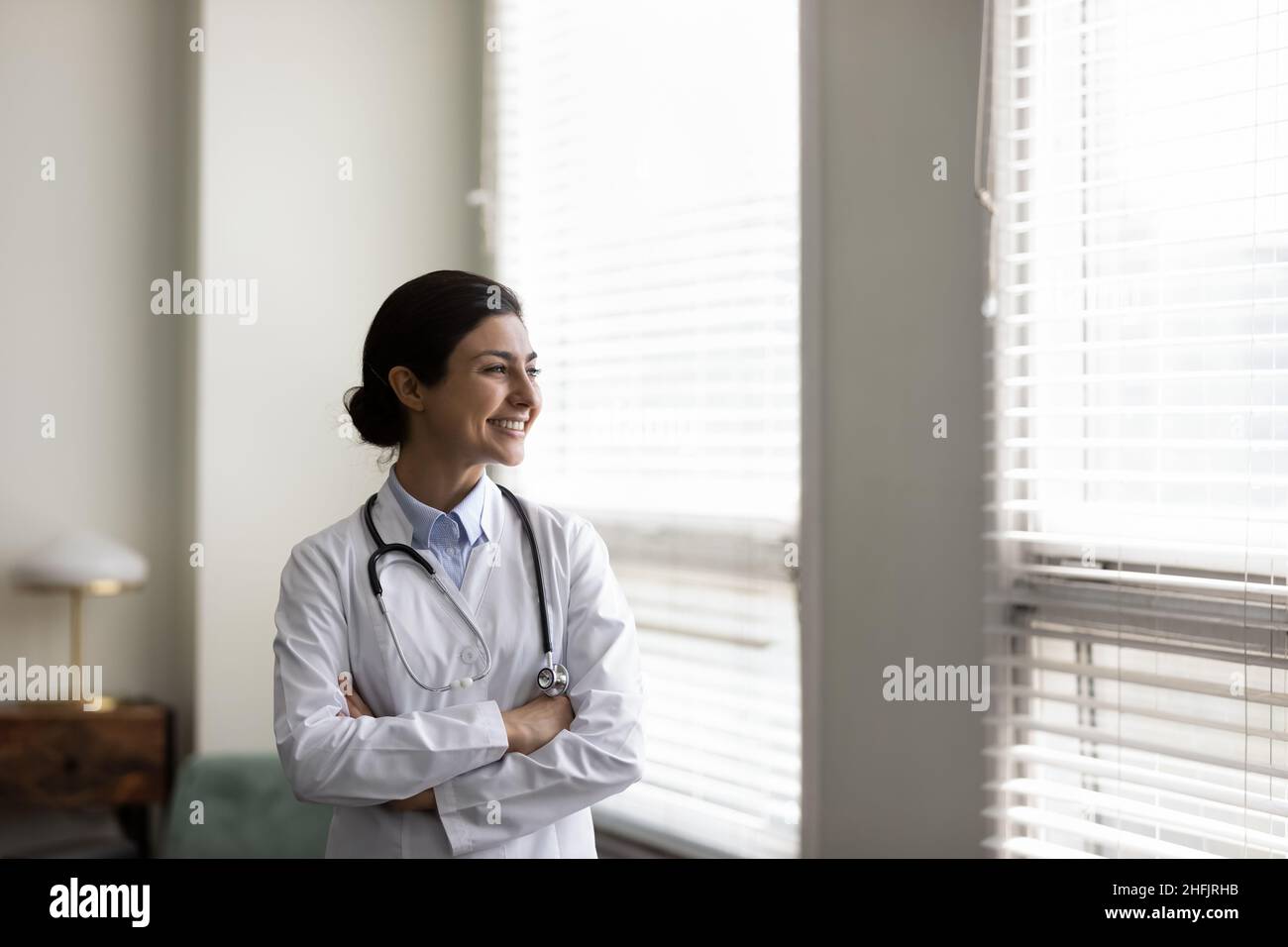 Selbstbewusster, glücklicher, junger indischer Arzt, der im Klinikbüro denkt. Stockfoto