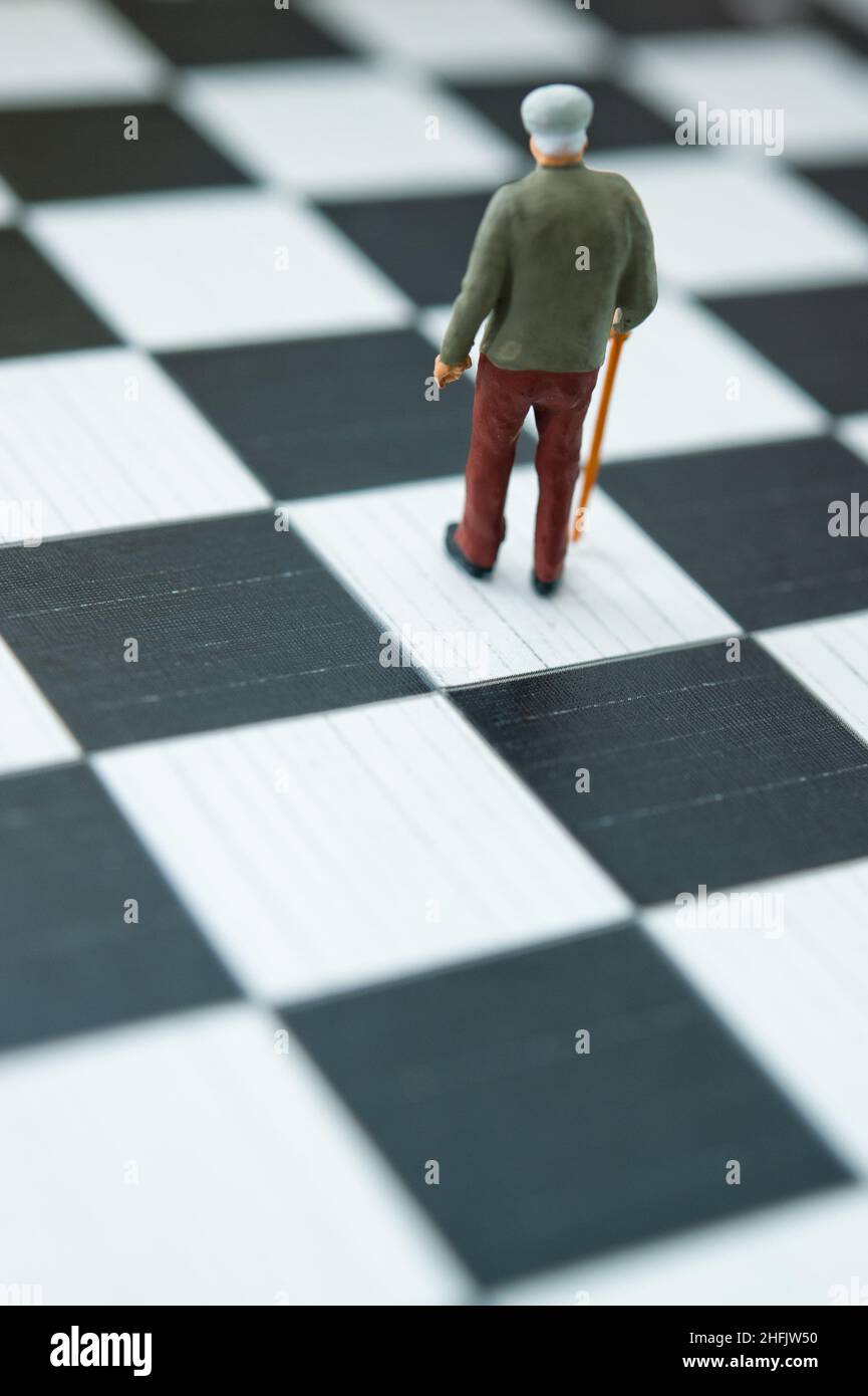 Miniaturfigur eines älteren Mannes mit Stock auf einem Schachbrett, Altern und Alterskonzept Stockfoto