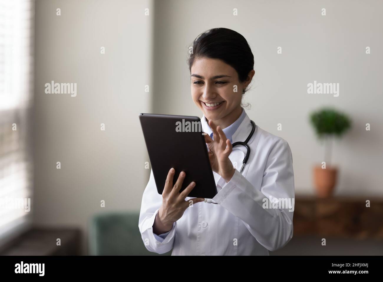 Glücklicher junger indischer Arzt mit digitaler Tablette. Stockfoto