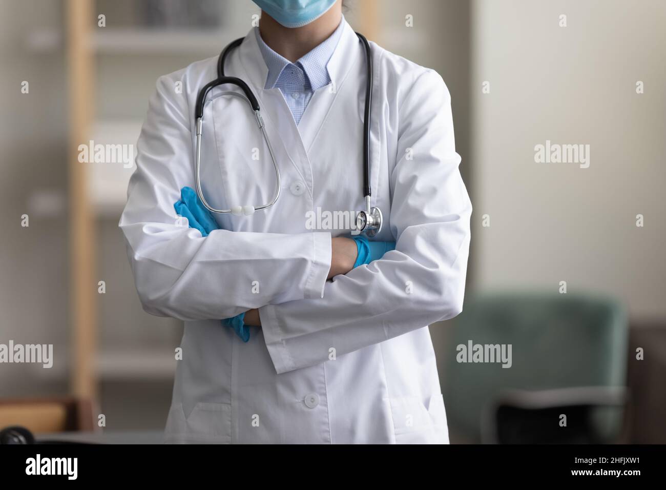 Beschnittenes Bild junge Ärztin, die mit gefalteten Armen steht. Stockfoto