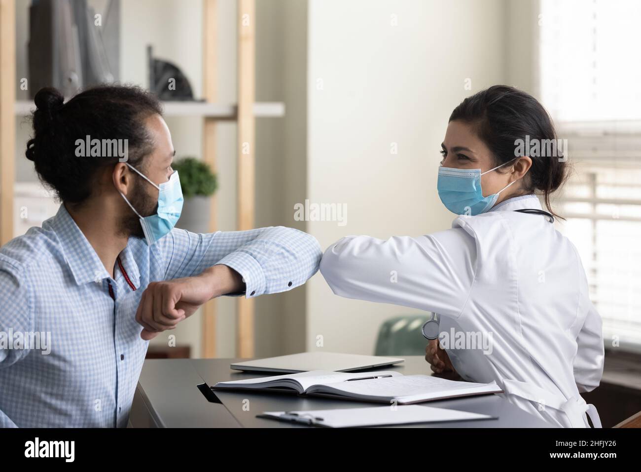 Glücklicher junger afroamerikanischer Patient, der mit dem indischen Arzt Ellbogen berührt. Stockfoto