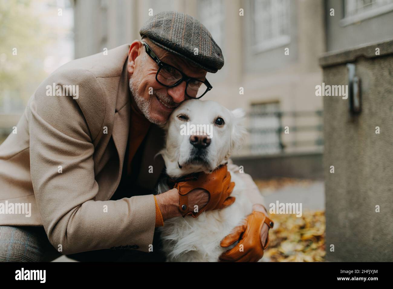 Glücklicher älterer Mann, der die Kamera anschaut und seinen Hund umarmt, während er draußen in der Stadt spazieren geht. Stockfoto